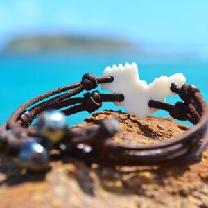 Bracelet avec un coquillage en forme de Saint-Barthélemy et deux perles de Tahiti présenté sur une roche face à la mer