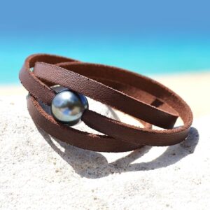 Brown flat leather bracelet with two Tahitian cultured pearls displayed on a rock by the sea