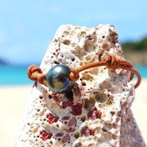 Adjustable brown leather bracelet with a 13.5 mm Tahitian cultured pearl displayed on a rock with a white flower
