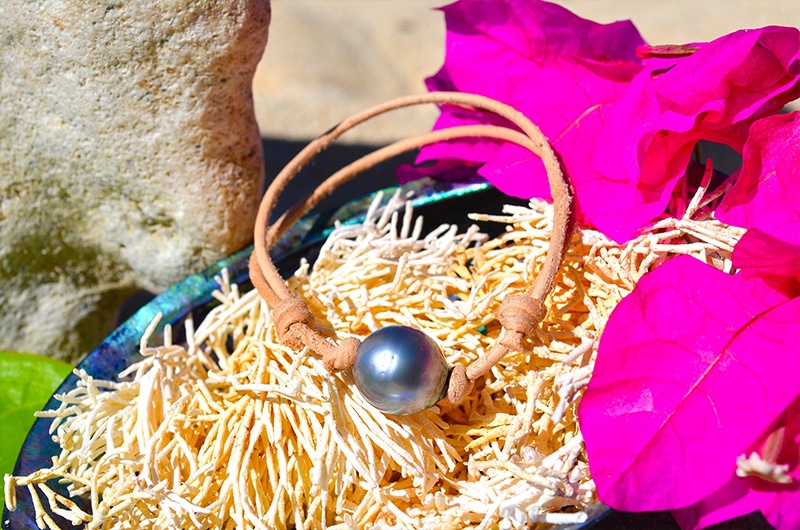 Bracelet ajustable en cuir avec une perle de Tahiti cerclée de 13 mm présenté sur un coquillage avec une fleur rose