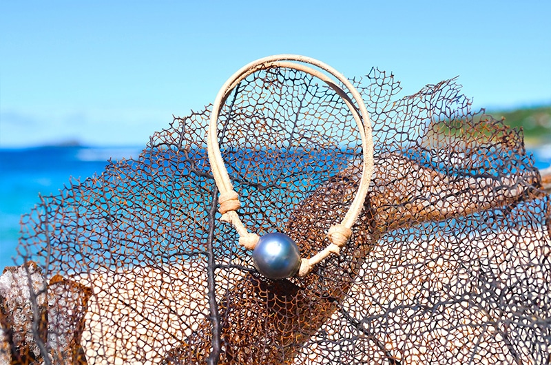 Bracelet ajustable en cuir avec une perle de Tahiti cerclée de 13 mm présenté sur un filet face à la mer