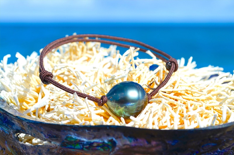 Adjustable bracelet with a 13 mm circled Tahitian pearl displayed on a shell by the sea