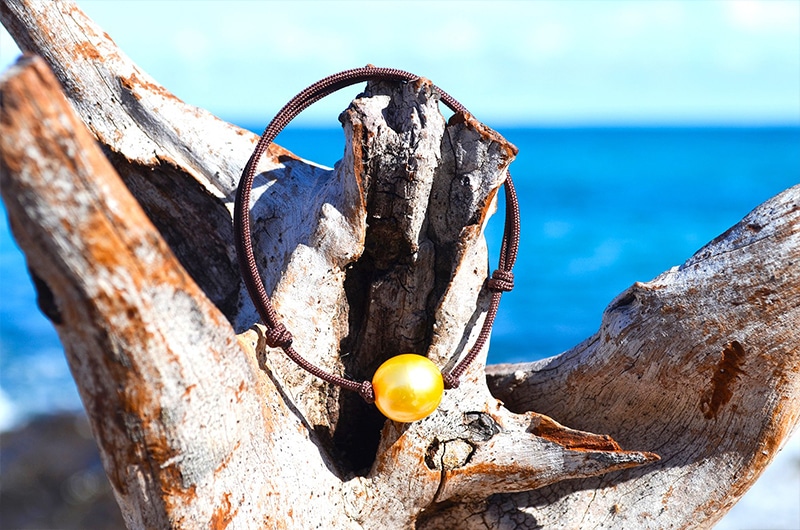 Vue d’ensemble du bracelet ajustable avec une perle dorée d’Australie de 11,5 mm présenté sur du bois face à la mer
