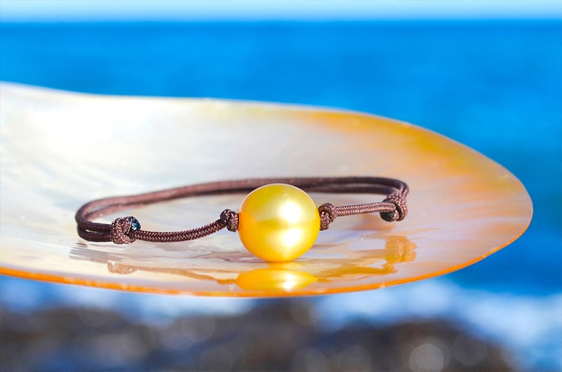 Bracelet ajustable avec une perle dorée d’Australie de 11,5 mm présenté sur une nacre face à la mer