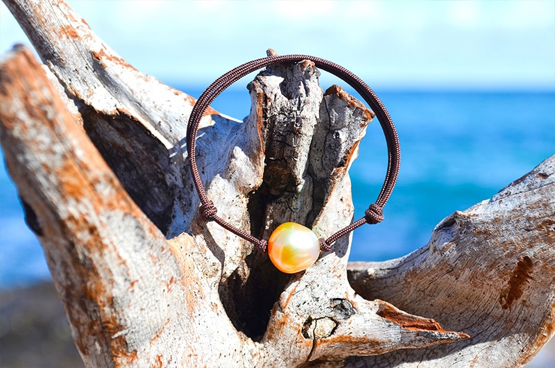 Vue d’ensemble du bracelet ajustable avec une perle dorée d’Australie de 12 mm présenté sur du bois face à la mer