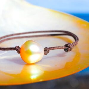 Bracelet ajustable avec une perle dorée d’Australie de 12 mm présenté sur une nacre face à la mer