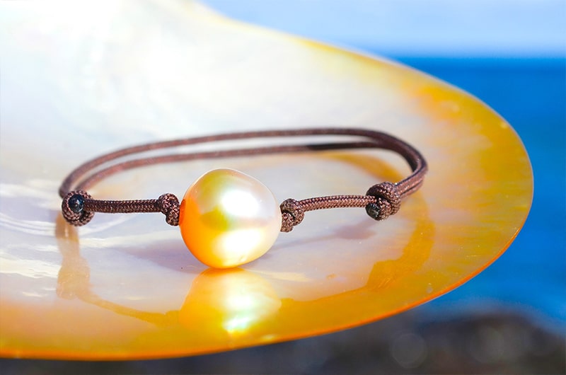 Bracelet ajustable avec une perle dorée d’Australie de 12 mm présenté sur une nacre face à la mer