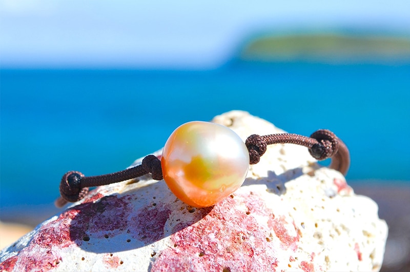 Bracelet ajustable avec une perle dorée d’Australie de 12 mm présenté sur une roche face à la mer