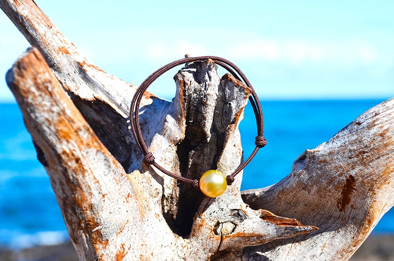 Vue d’ensemble du bracelet ajustable avec une perle dorée d’Australie de 9 mm présenté sur du bois face à la mer