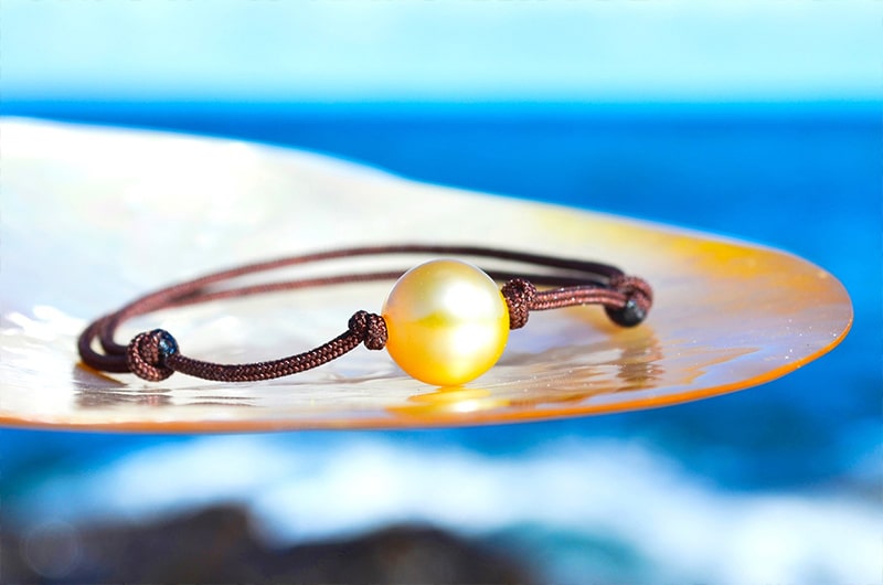 Bracelet ajustable avec une perle dorée d’Australie de 9 mm présenté sur une nacre face à la mer