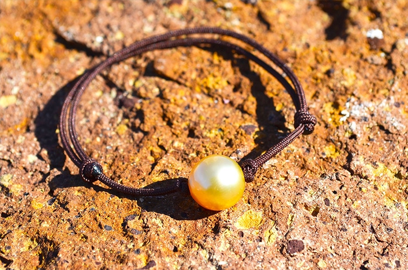 Bracelet ajustable avec une perle dorée d’Australie de 9 mm présenté sur une roche