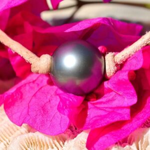 Detail of the 12.5 mm round Tahitian pearl on the leather bracelet displayed with pink flowers