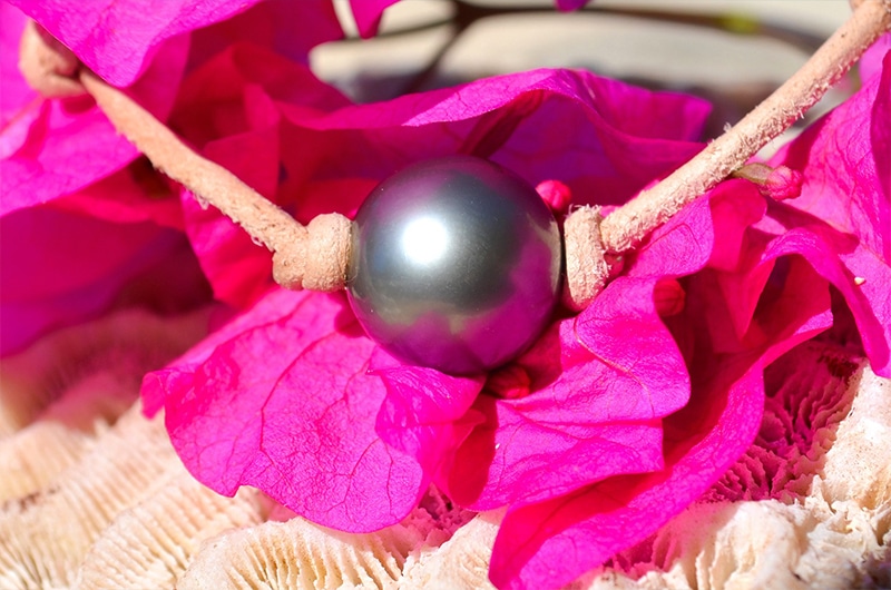 Detail of the 12.5 mm round Tahitian pearl on the leather bracelet displayed with pink flowers