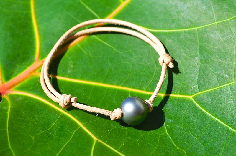 Full view of the adjustable leather bracelet with a 12.5 mm round Tahitian pearl displayed on a green leaf