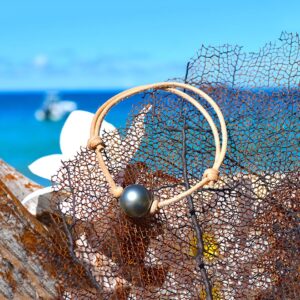 Adjustable brown leather bracelet with a 12.5 mm round Tahitian cultured pearl displayed on a net by the sea