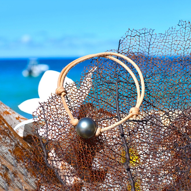 Adjustable brown leather bracelet with a 12.5 mm round Tahitian cultured pearl displayed on a net by the sea