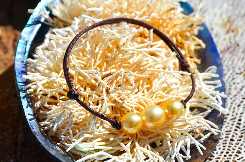 Vue d’ensemble du bracelet ajustable avec trois perles dorées d’Australie de 8,5 mm présenté sur un coquillage