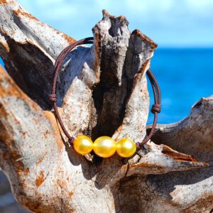 Bracelet ajustable sur cordon marron avec trois perles de culture dorées d’Australie de 8,5 mm présenté sur du bois face à la mer
