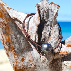 Full view of the adjustable bracelet with a 12.5 mm circled Tahitian pearl displayed on wood by the sea