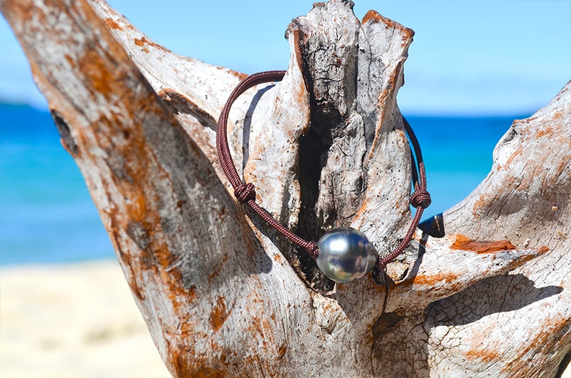 Vue d’ensemble du bracelet ajustable avec une perle de Tahiti cerclée de 12,5 mm présenté sur du bois face à la mer