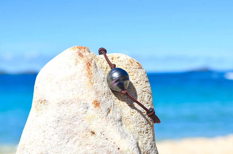Détail de la perle de Tahiti cerclée de 12,5 mm sur le bracelet ajustable présenté sur une roche face à la mer