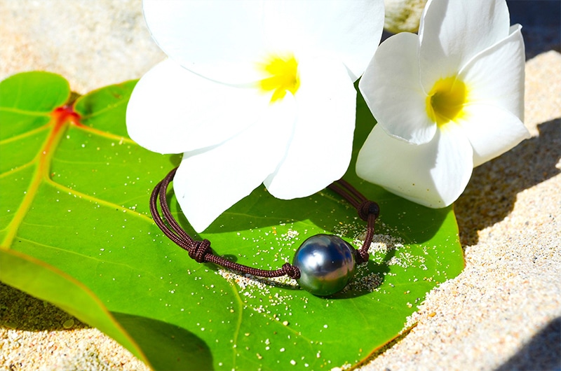 Bracelet ajustable avec une perle de Tahiti cerclée de 12,5 mm présenté sur une feuille avec des fleurs blanches