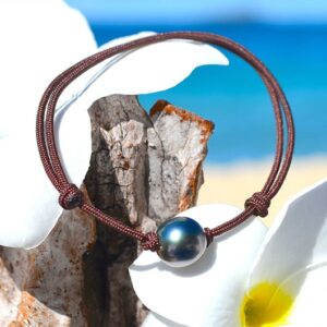 Adjustable bracelet with a 9 mm semi-round Tahitian pearl displayed on wood with white flowers by the sea