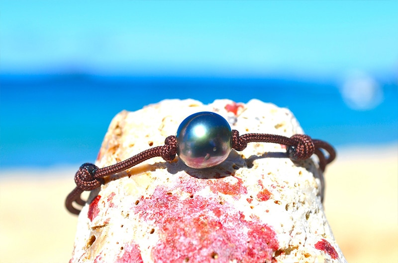 Détail de la perle semi-ronde de Tahiti de 9 mm sur le bracelet ajustable présenté sur une roche face à la mer