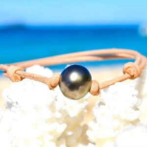 Adjustable leather bracelet with a 12 mm semi-round Tahitian pearl displayed on white coral by the sea
