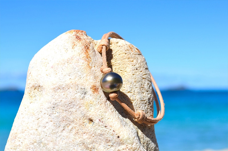 Detail of the 12 mm semi-round Tahitian pearl on the leather bracelet displayed on a rock by the sea