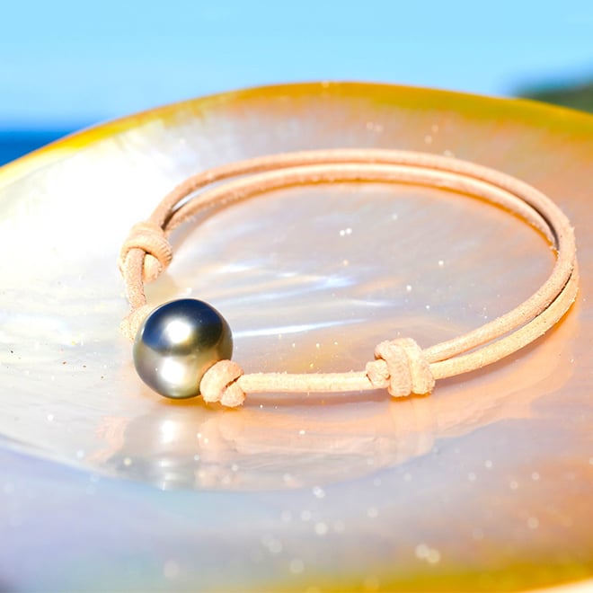 Adjustable brown leather bracelet with a 12 mm semi-round Tahitian cultured pearl displayed on mother-of-pearl by the sea