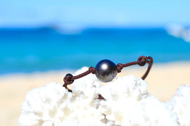 Detail of the 9.5 mm semi-round Tahitian pearl on the adjustable bracelet displayed on white coral by the sea