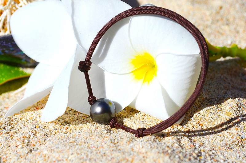 Full view of the adjustable bracelet with a 9.5 mm semi-round Tahitian pearl displayed on a leaf with a white flower