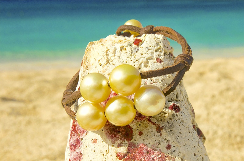 Bracelet en cuir avec cinq perles dorées d’Australie présenté sur une roche face à la mer