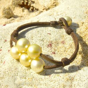 Bracelet en cuir marron avec cinq perles de culture dorées d’Australie présenté sur le sable