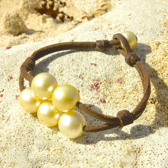 Bracelet en cuir marron avec cinq perles de culture dorées d’Australie présenté sur le sable