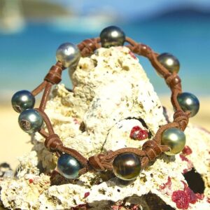 Leather bracelet with nine Tahitian pearls and knots displayed on a rock by the sea