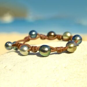 Brown leather bracelet with nine Tahitian cultured pearls separated by knots displayed on sand by the sea