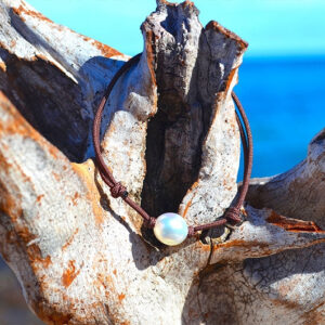 Bracelet ajustable en cordon marron avec perle blanche d’Australie, présenté sur du bois flotté face à la mer