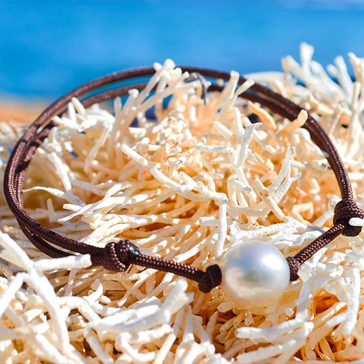 Adjustable bracelet with a white Australian cultured pearl, displayed on white coral by the sea