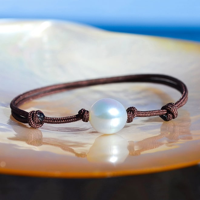 Adjustable brown cord bracelet with an 8.5 mm white Australian cultured pearl, displayed on a mother-of-pearl shell