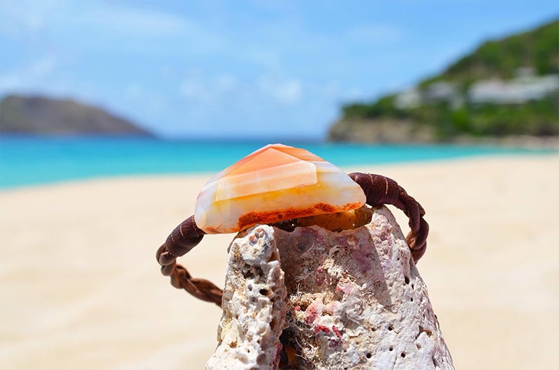 Detail of the orange agate and braided leather bracelet displayed on a rock by the sea