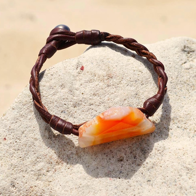 Brown braided leather bracelet with an orange agate and a Tahitian cultured pearl displayed on sand