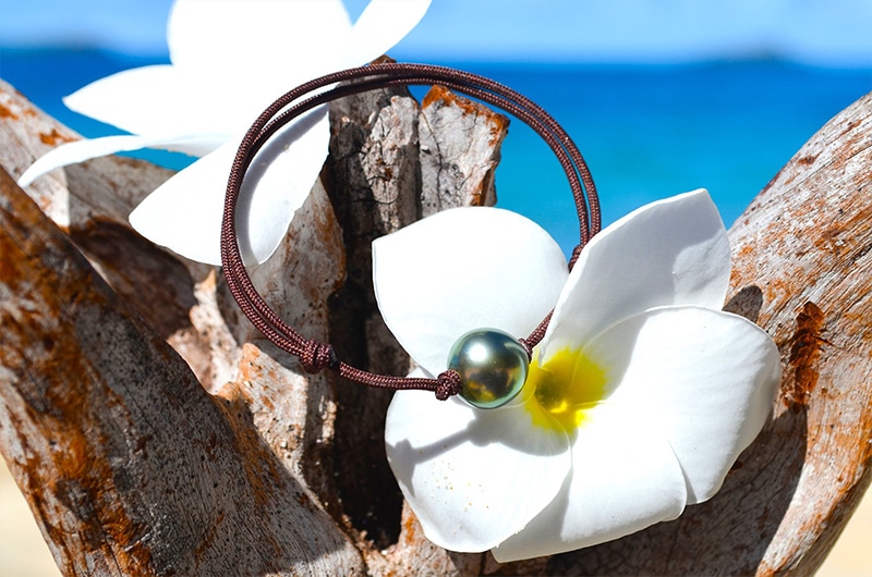 Full view of the adjustable bracelet with a 10.5 mm semi-round Tahitian pearl displayed on wood with a white flower by the sea