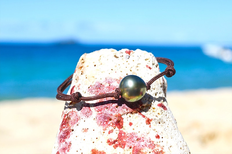 Adjustable bracelet with a 10.5 mm semi-round Tahitian pearl displayed on a rock by the sea