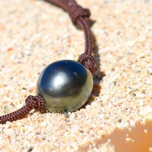 Detail of the 10 mm semi-round Tahitian pearl and adjustable cord displayed on sand