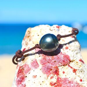 Detail of the 11.5 mm semi-baroque Tahitian pearl on the adjustable bracelet displayed on a rock by the sea