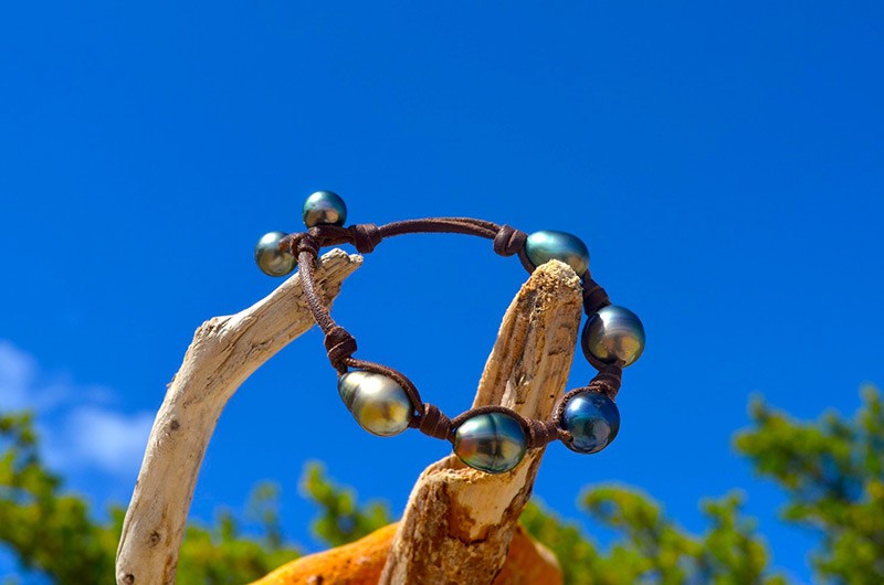 Full view of the bracelet with five baroque Tahitian pearls displayed on wood against a blue sky