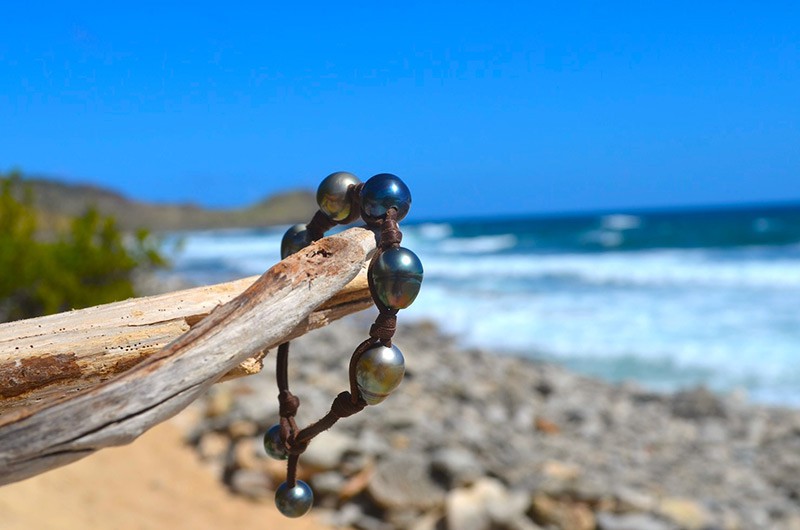 Leather bracelet with five baroque Tahitian pearls and two closure pearls displayed on wood by the sea