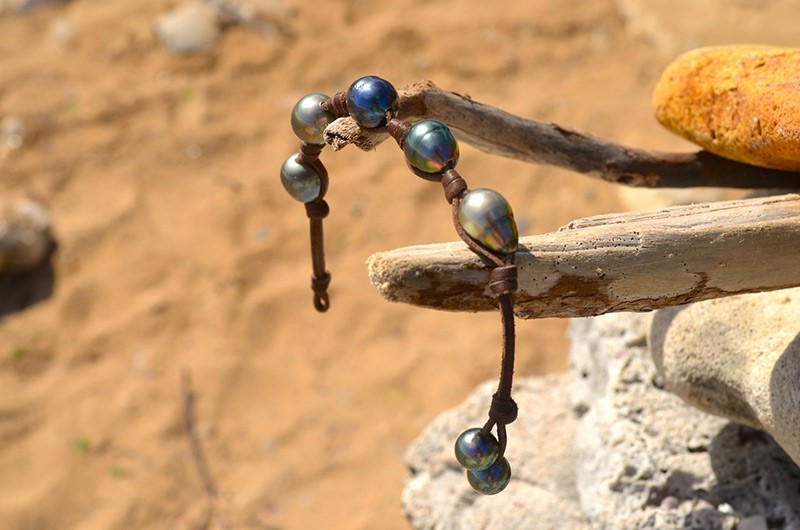 Leather bracelet with five baroque Tahitian pearls and two closure pearls displayed on wood and sand